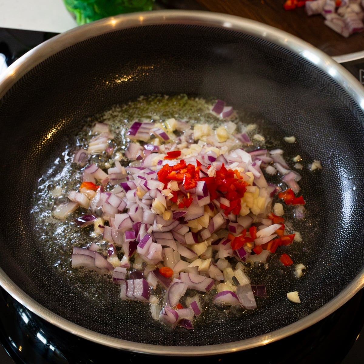 Red onion, garlic, and red chili cooking in butter for chicken sisig