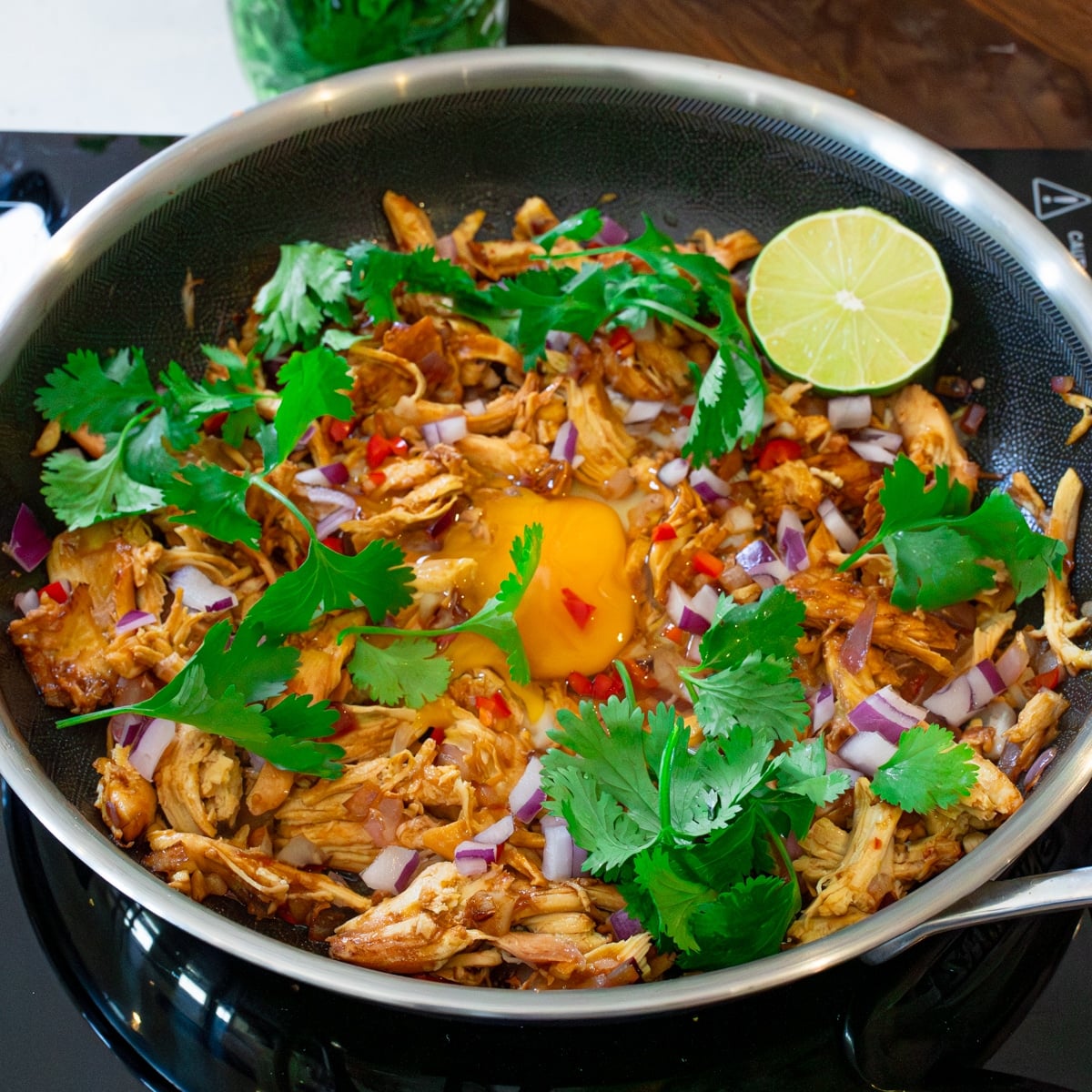 Filipino chicken sisig topped with a runny egg, red onion, cilantro, chili, and lime