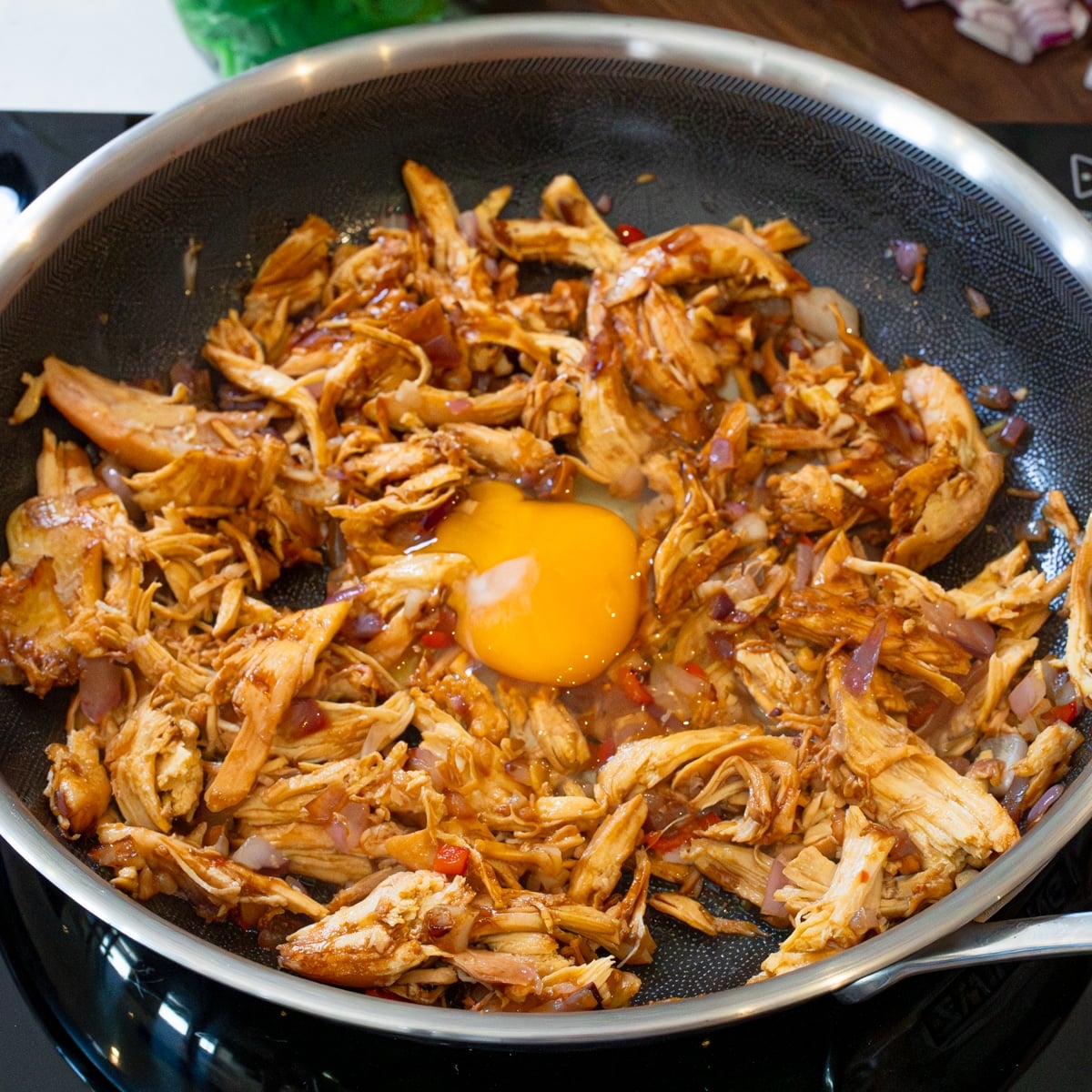 An egg cracked over sizzling chicken sisig in a skillet