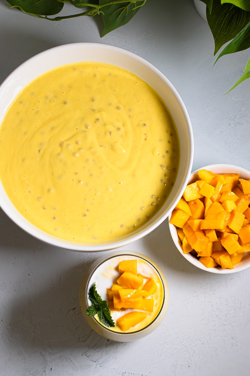 Overhead view of mango sago in a bowl with a serving glass and fresh cubed mango
