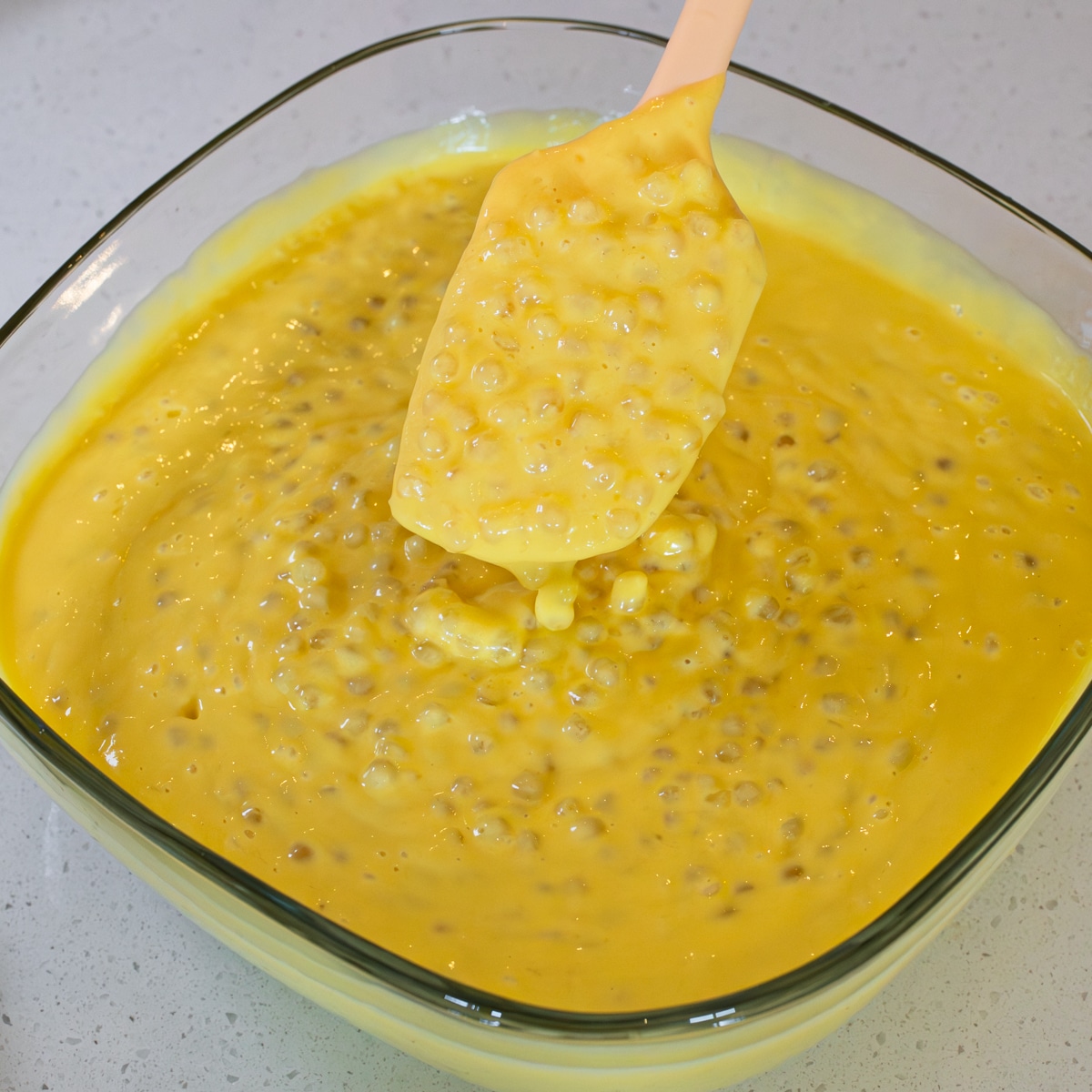 Mango sago mixed with sago pearls in a bowl, lifted on a spatula
