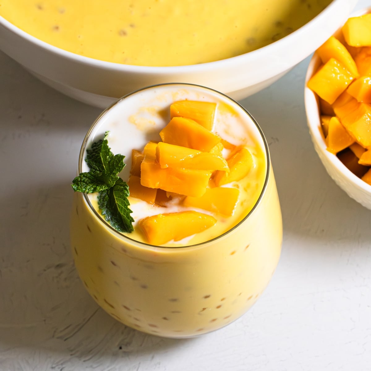 Cool, creamy mango sago in a glass topped with fresh mango cubes and mint