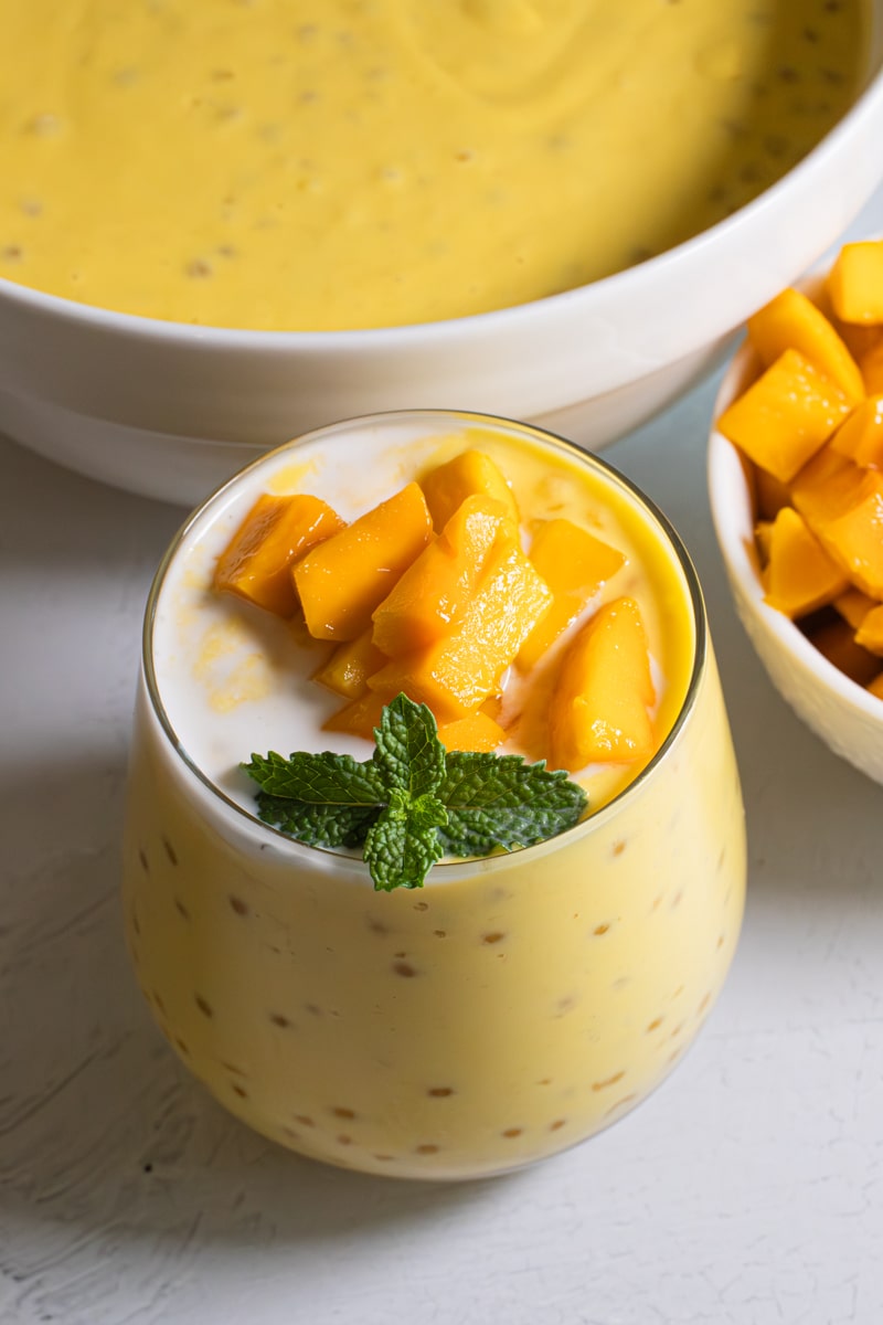 Close-up of creamy mango sago in a glass topped with fresh mango and mint