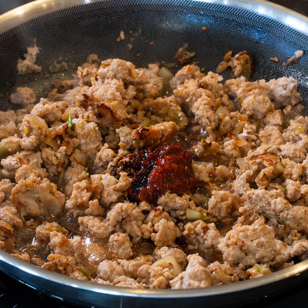 Ground chicken cooking in a pan with garlic, ginger, green onions, and doubanjiang for chicken miso ramen topping