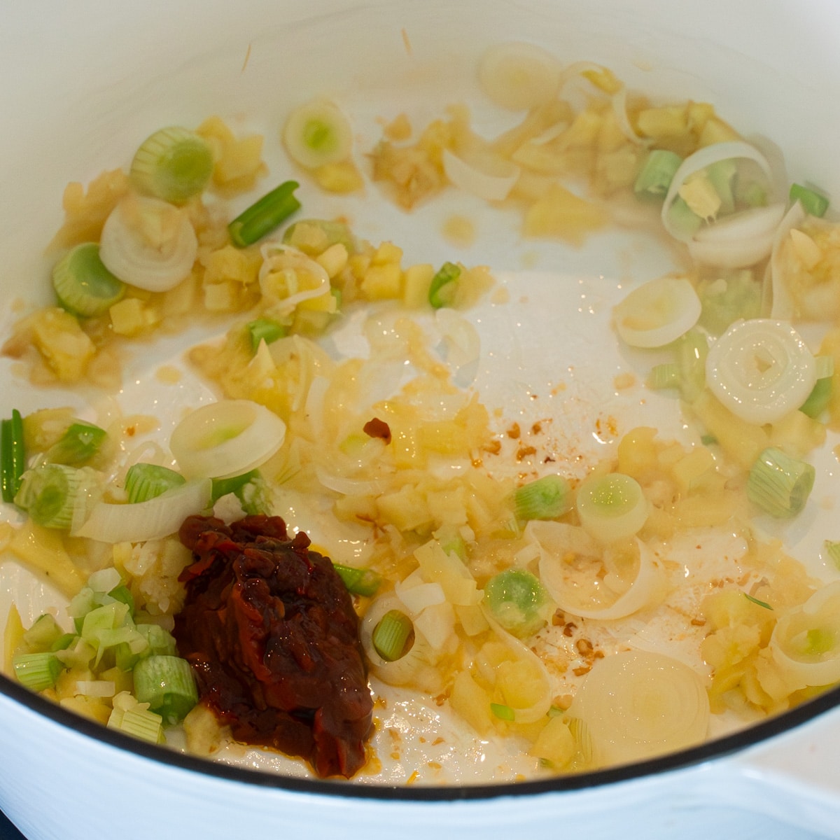 Garlic, ginger, green onions, and doubanjiang sauteing in a white pot to build the miso ramen broth base