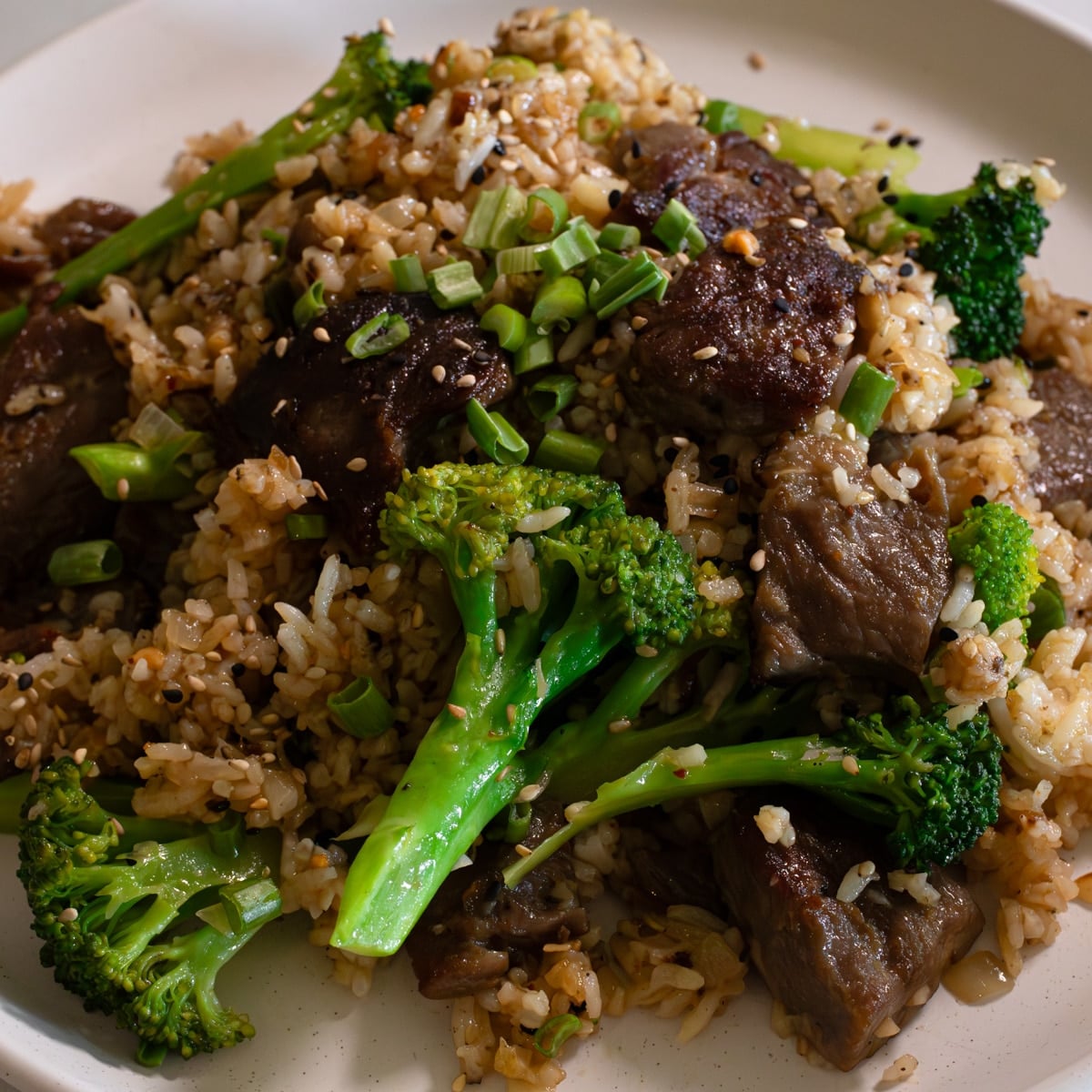 Beef and broccoli fried rice with velveted beef strips broccoli florets green onions and sesame seeds on a plate