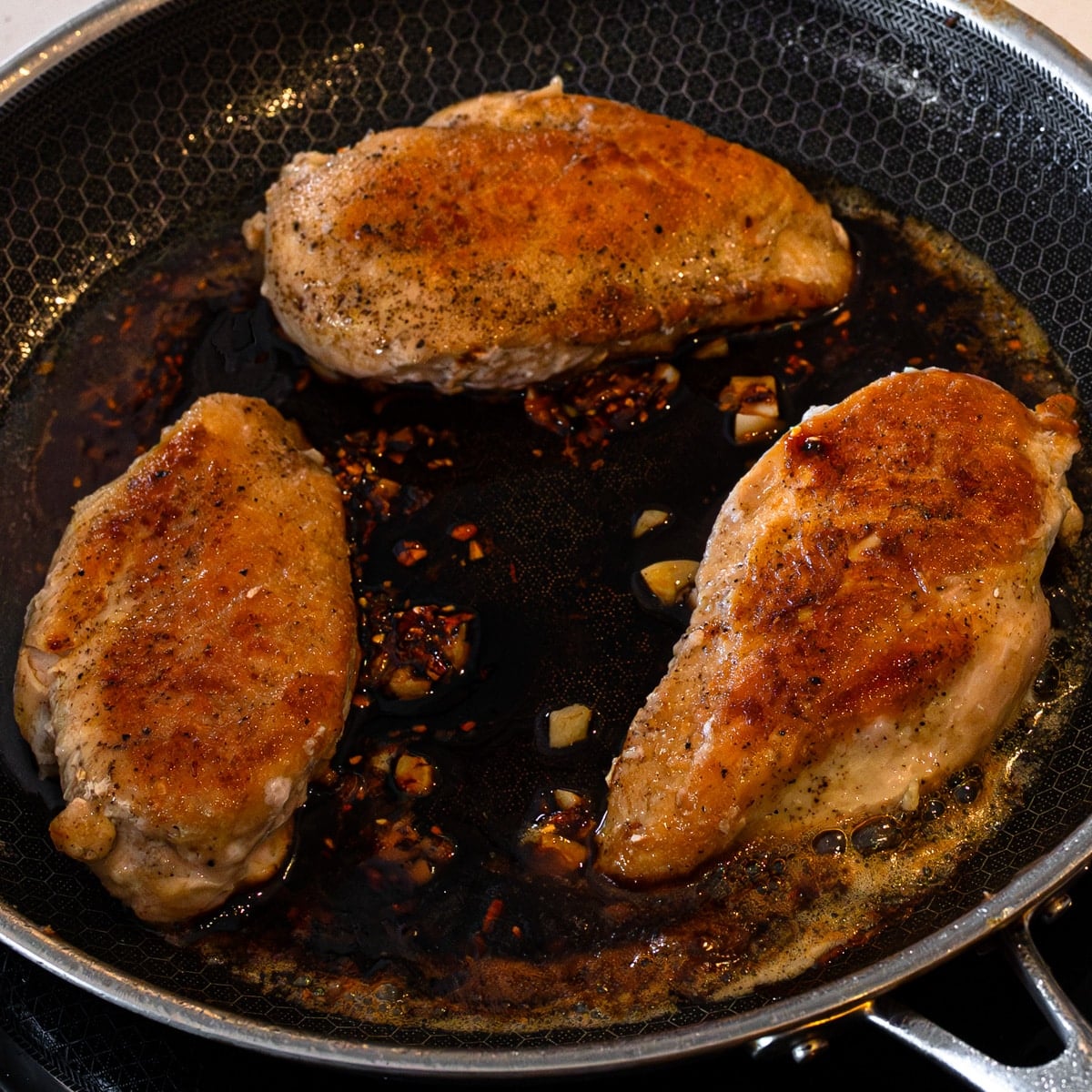 Soy sauce, dark soy, maple syrup, chili crunch, and lime added to the skillet to build the sticky maple glaze