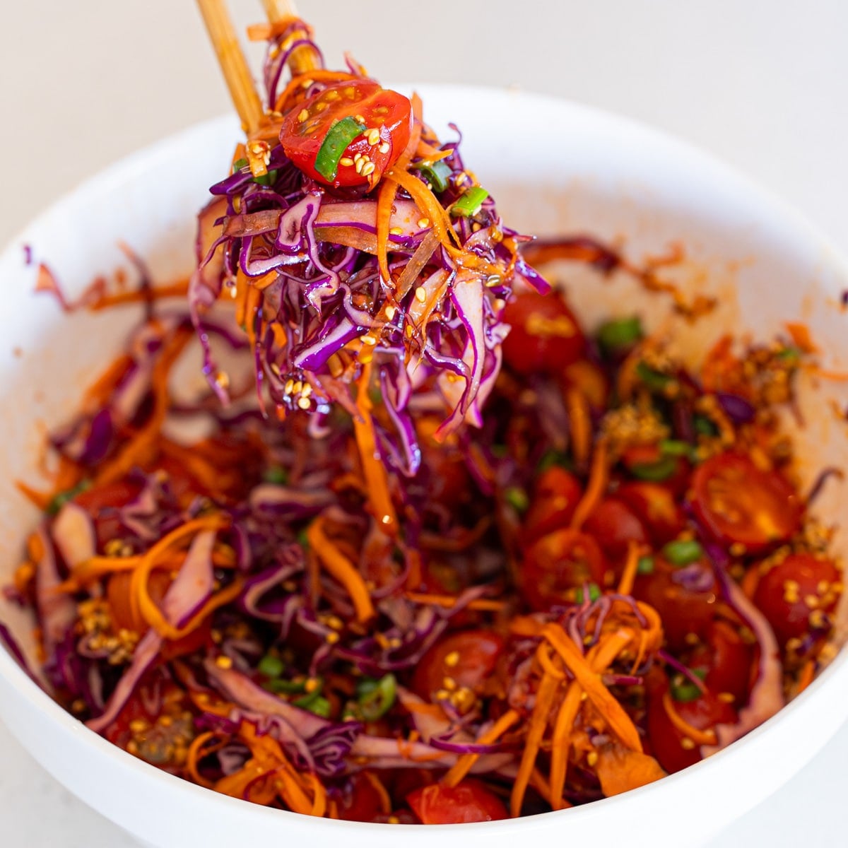 Purple cabbage, carrots, and tomatoes tossed in honey soy dressing in a white bowl
