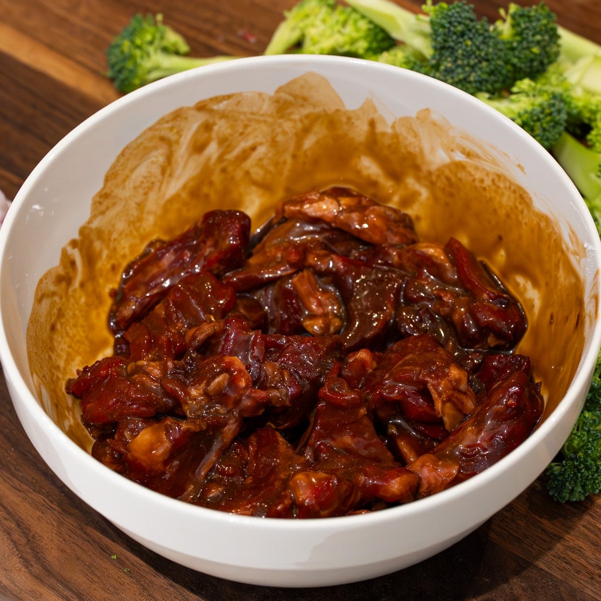 Velveted beef strips coated in cornstarch baking soda soy sauce and oyster sauce in a white bowl ready to sear