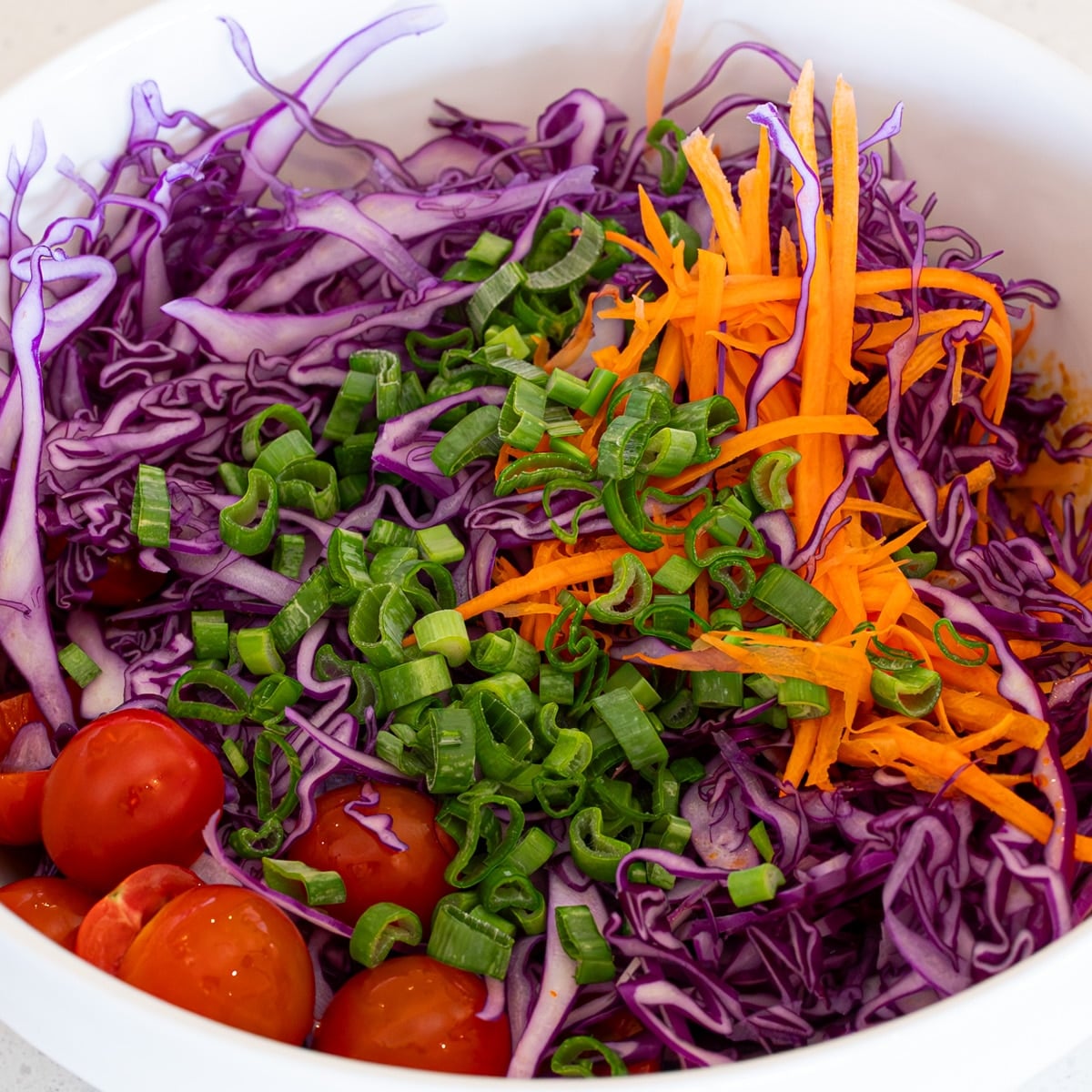 Shredded purple cabbage, carrots, green onion, and halved cherry tomatoes in a white bowl for dumpling salad