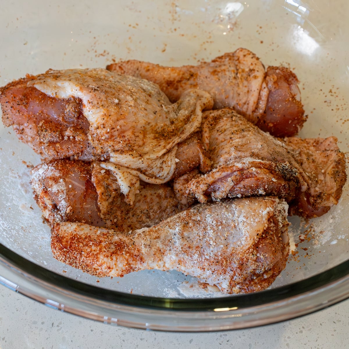 Chicken pieces seasoned with paprika, garlic powder, salt, and pepper in a glass bowl