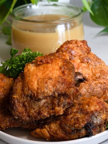 Crispy air fryer Jollibee fried chicken stacked on a white plate with parsley and a jar of brown gravy behind