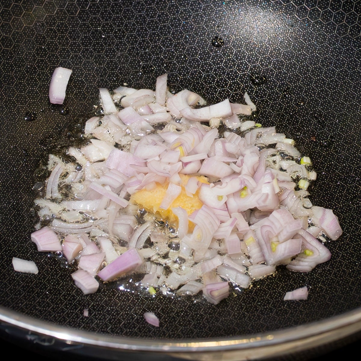 Shallot and minced garlic sauteing in a hot wok with oil for beef and broccoli fried rice