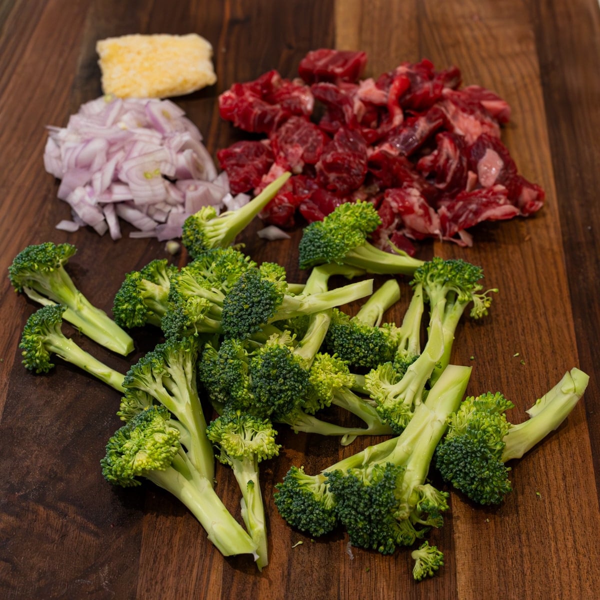 Raw beef strips broccoli florets shallot and minced garlic prepped on a wooden cutting board for beef and broccoli fried rice