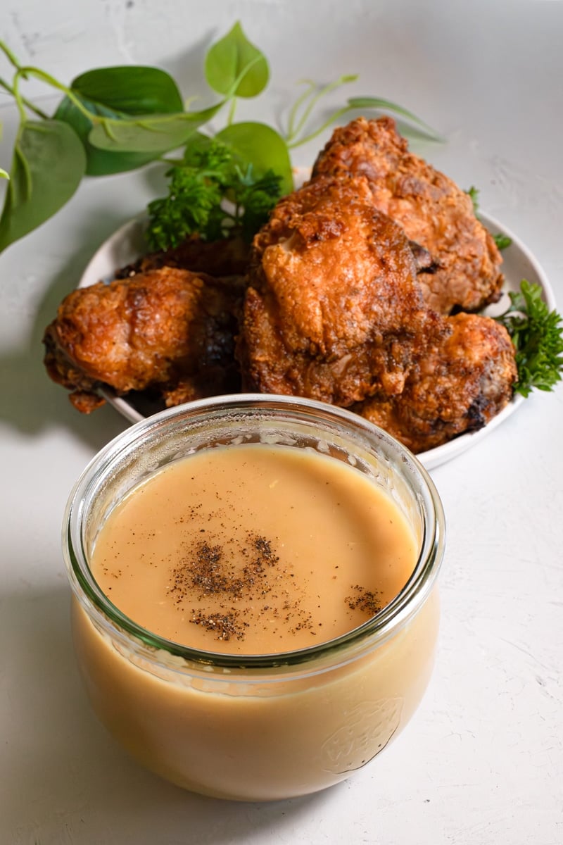 Golden crispy Jollibee fried chicken on a plate with a jar of homemade brown gravy and black pepper