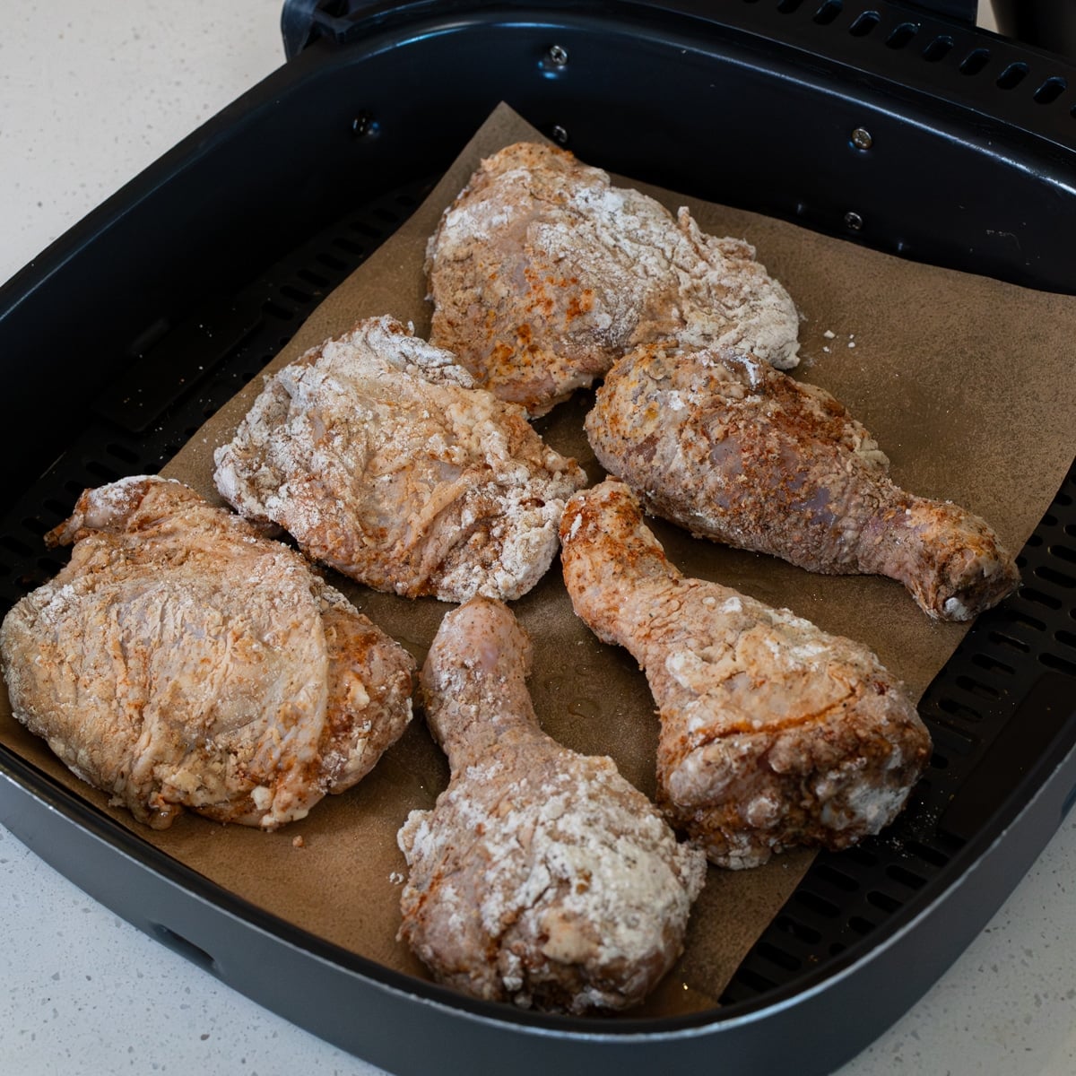 Coated chicken placed skin side down in an air fryer basket before cooking