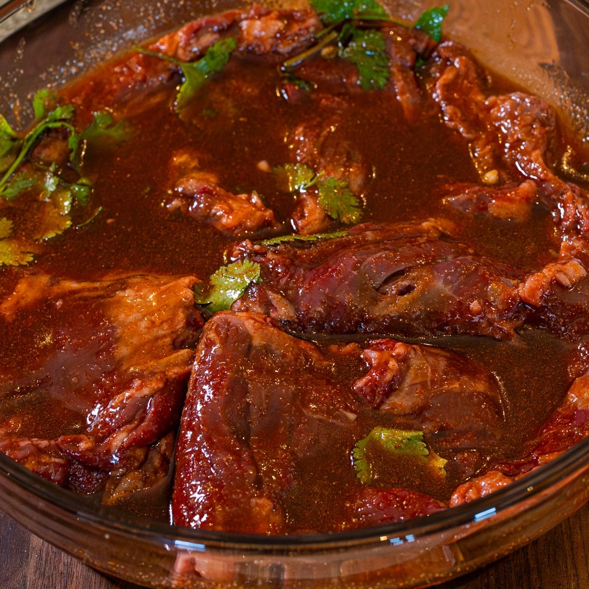Skirt steak coated in honey sriracha marinade in a glass dish ready to refrigerate for 1 hour