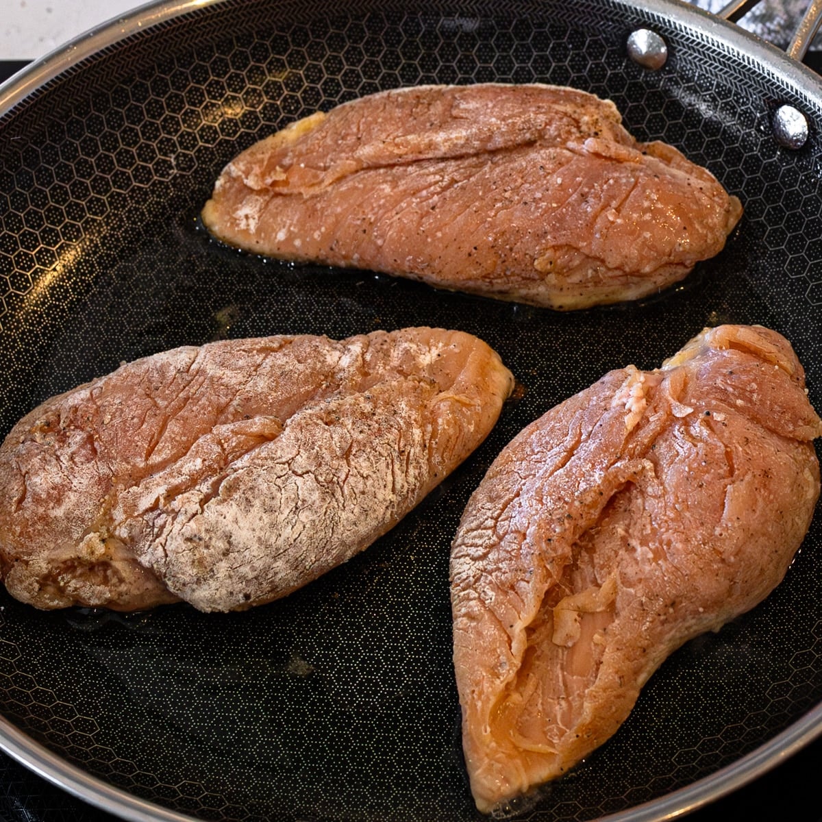 Chicken breasts seasoned with salt, pepper, and flour ready to pan fry for maple glazed chicken