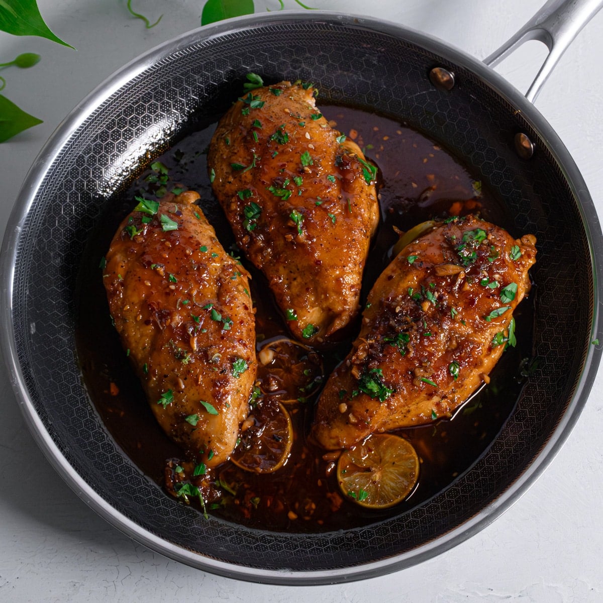 Maple glazed chicken breasts in a sticky soy chili crunch glaze with lime slices and fresh cilantro in a HexClad skillet