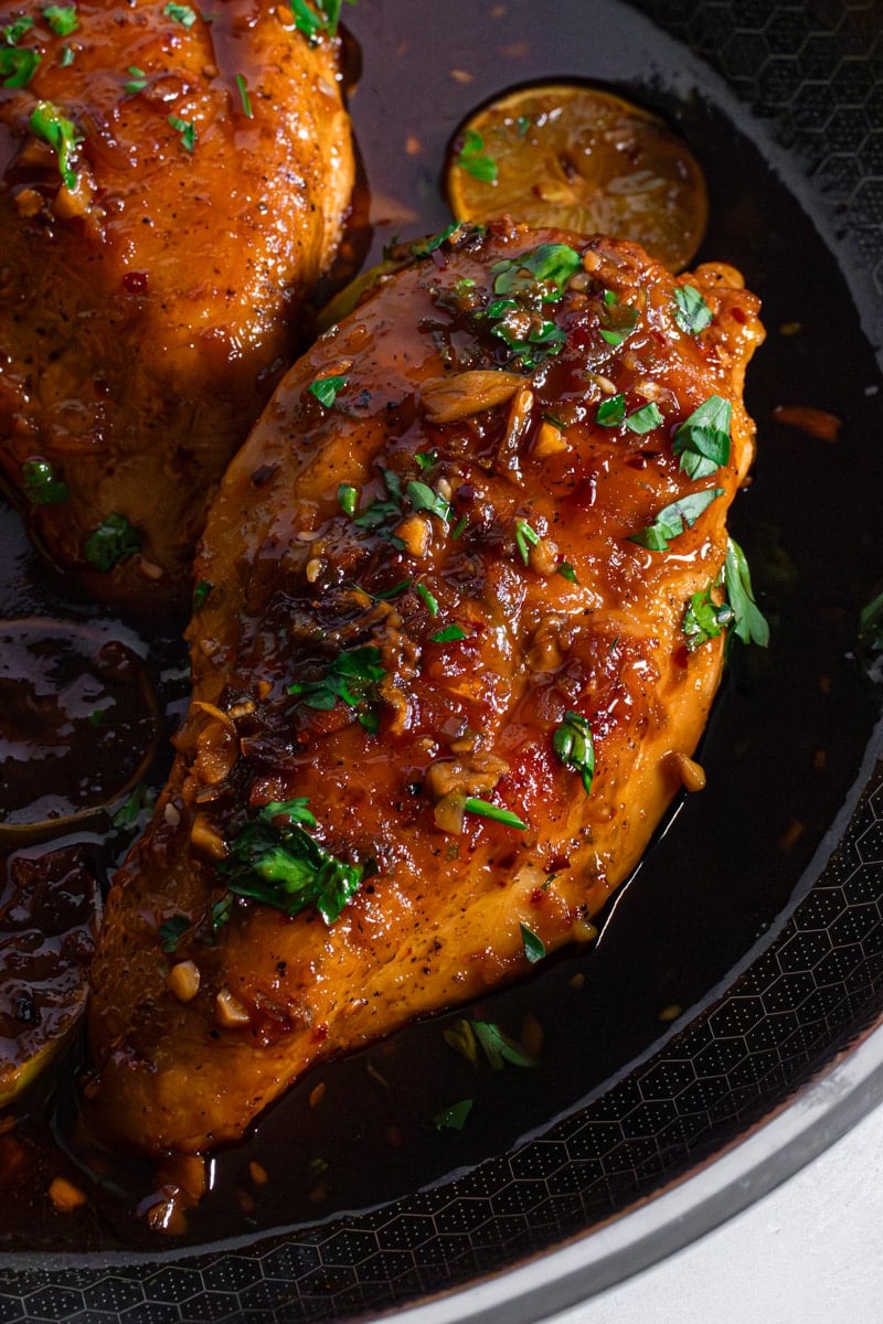 Close up of maple glazed chicken breast with sticky soy chili crunch glaze, crispy garlic, and fresh cilantro in a skillet