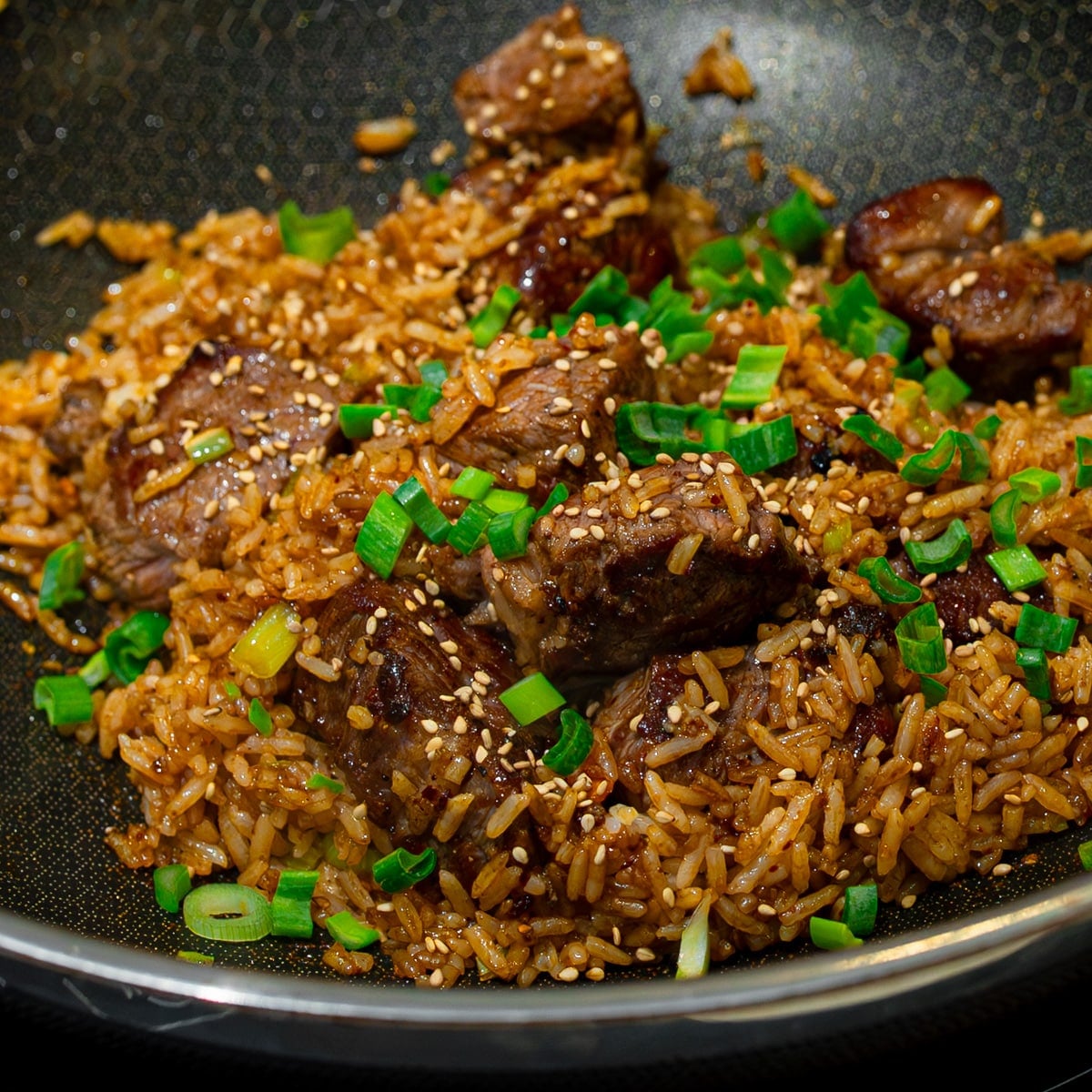 Steak fried rice tossed with green onion and sesame in a wok