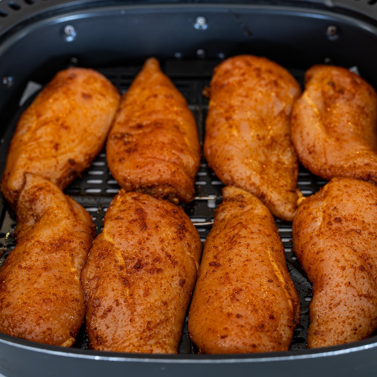 Marinated chicken breasts arranged in a single layer in an air fryer basket