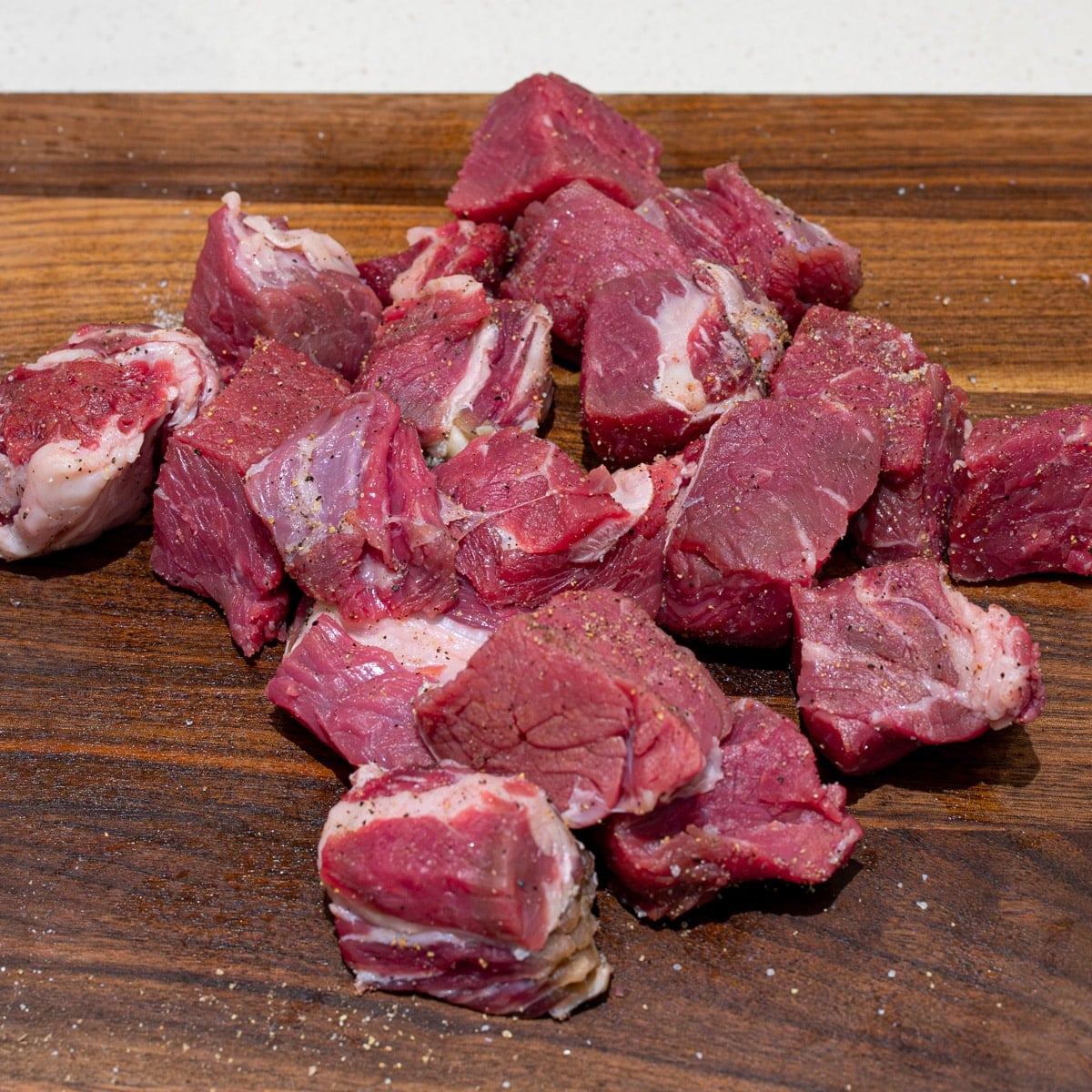 Cubed ribeye steak seasoned with salt and pepper on a cutting board