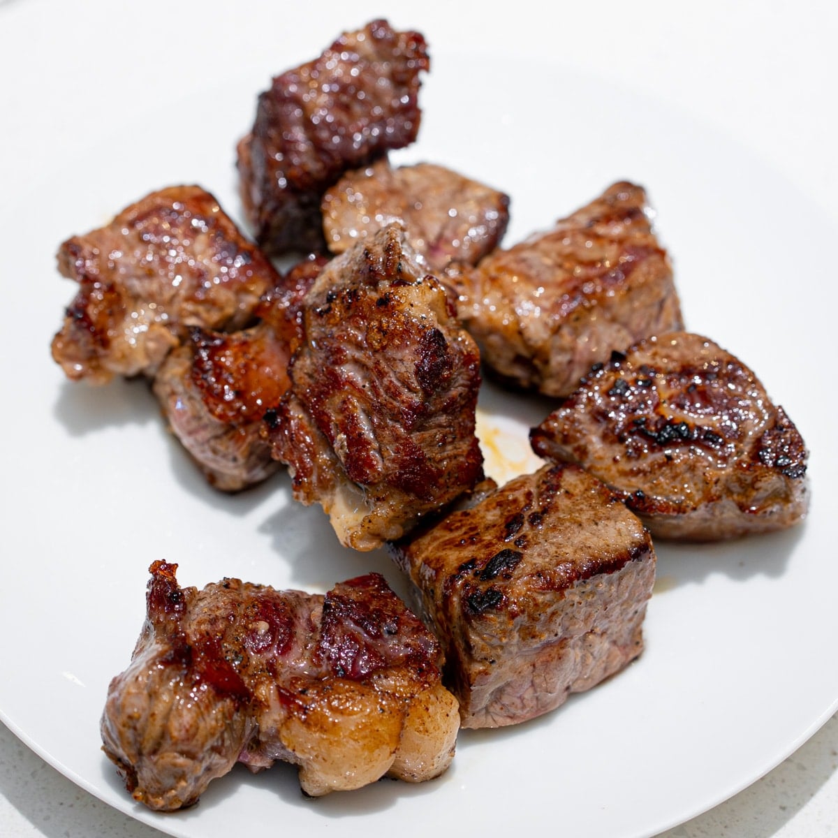 Seared ribeye steak cubes resting on a white plate