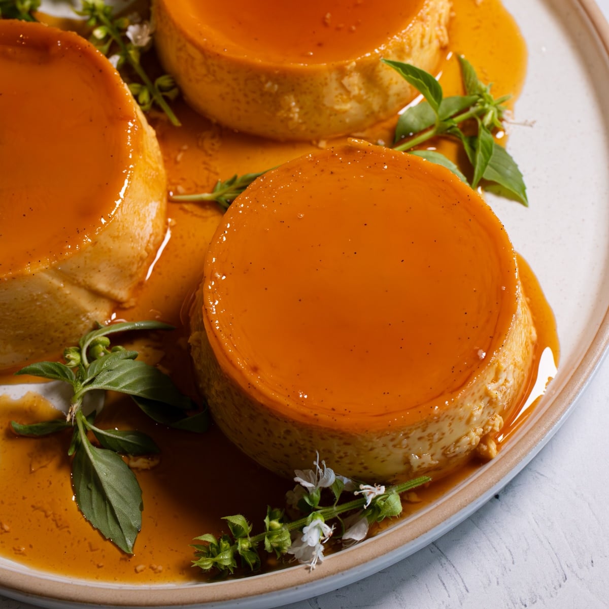 overhead close up of 3 filipino leche flan custards topped with golden caramel sauce and plated with fresh herbs