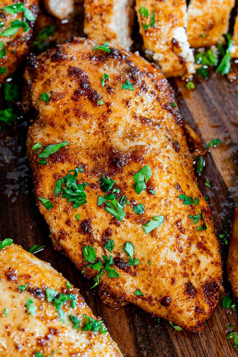 Close-up of a juicy air fryer chicken breast with a smoky spice crust and fresh parsley on a wood board