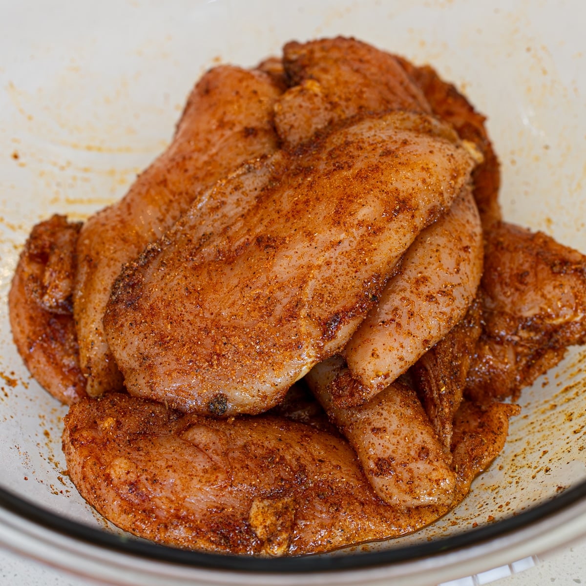 Chicken breasts coated in olive oil and a smoky spice marinade in a glass bowl
