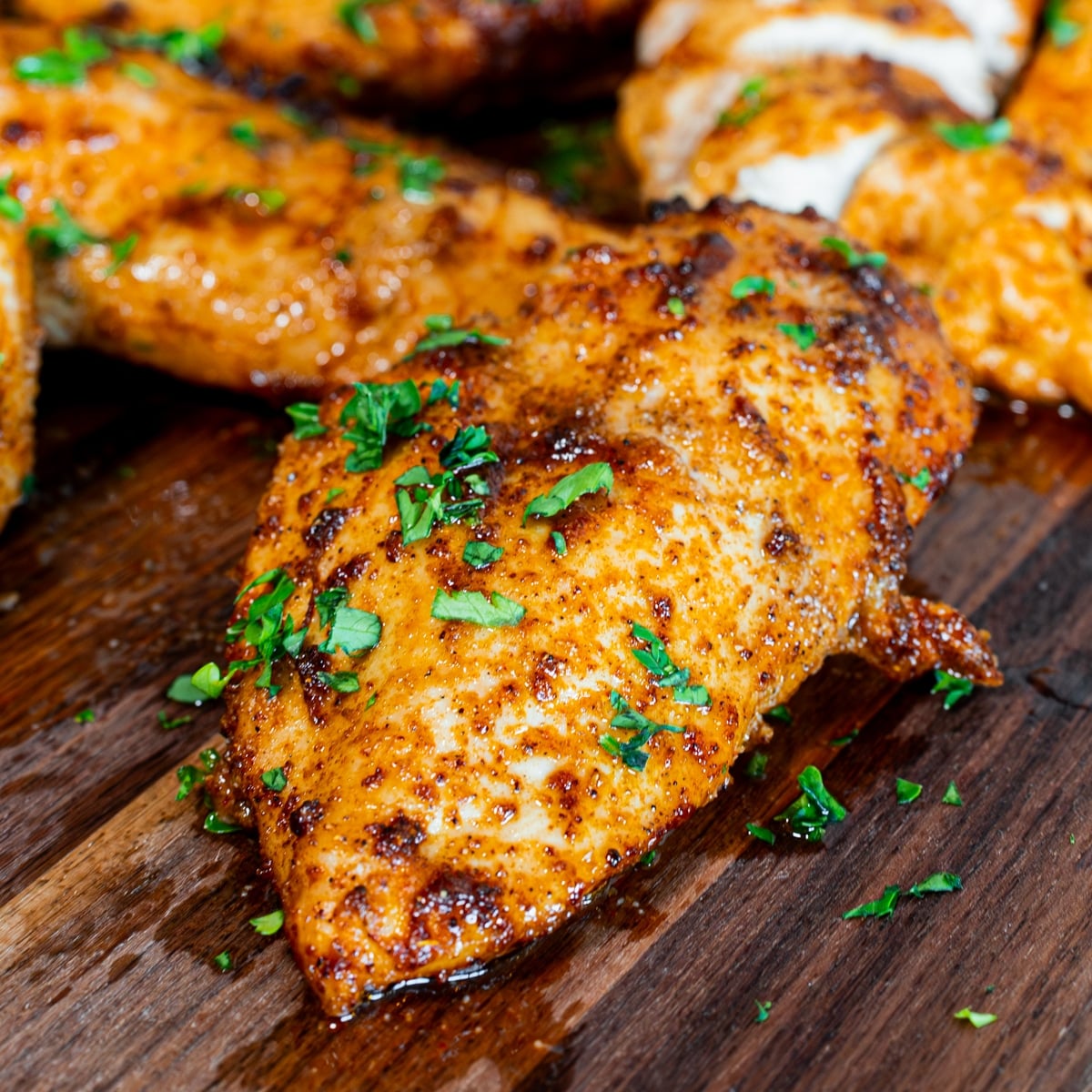 Juicy sliced air fryer chicken breast on a wood board garnished with parsley