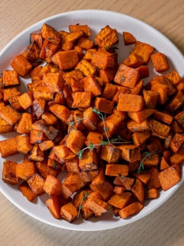 Crispy sweet potatoes air fryer recipe served on a white plate with fresh thyme